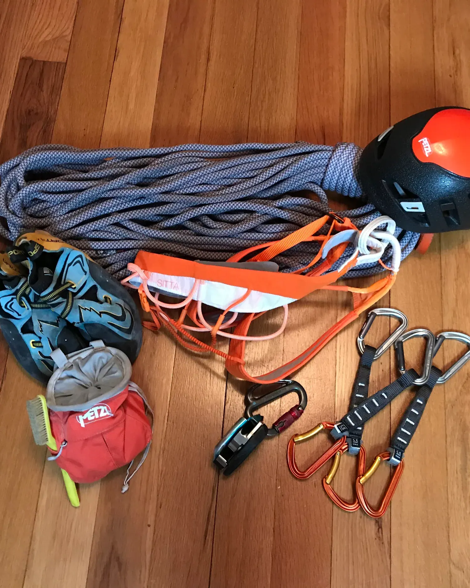 A climbing rope coiled beside a helmet, harness, shoes and quickdraws